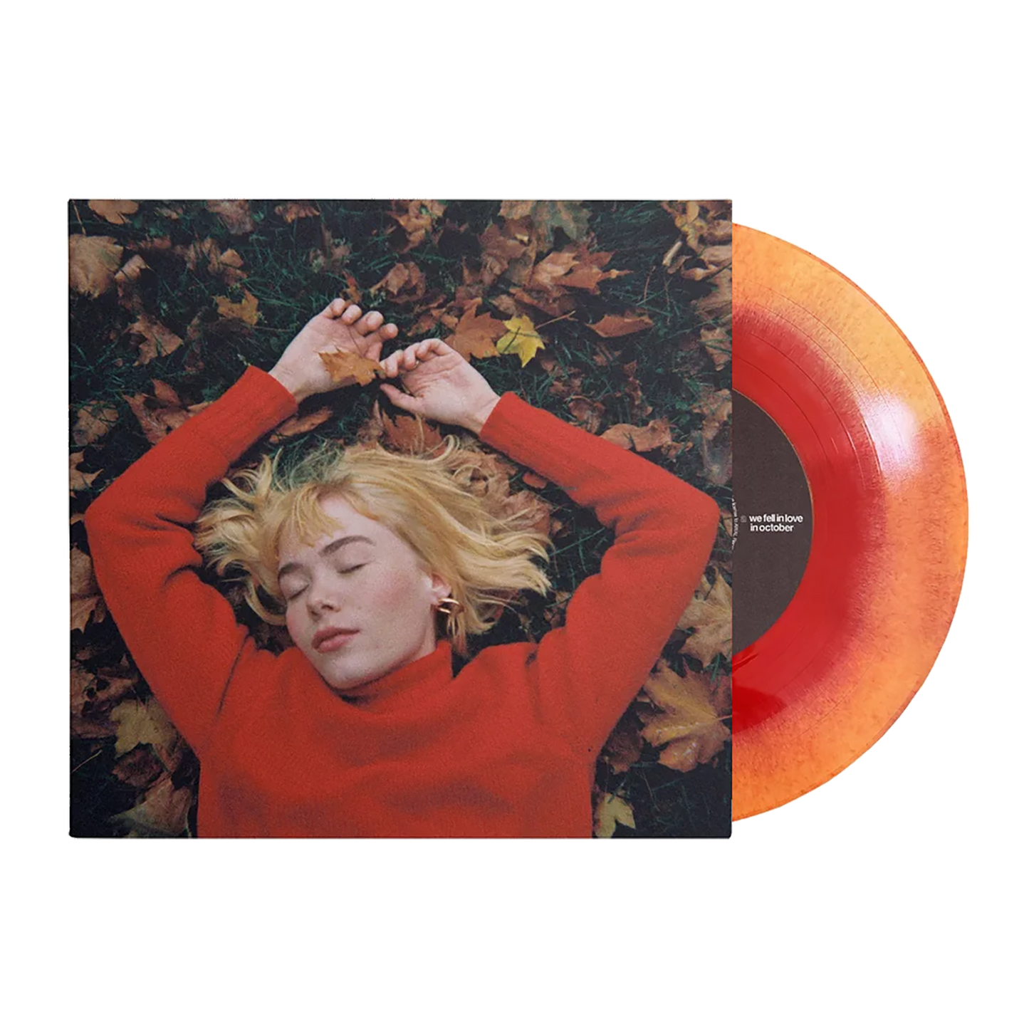 A person lying on leaves with their hands above their head, wearing a red sweater, with a orange and yellow vinyl record alongside.