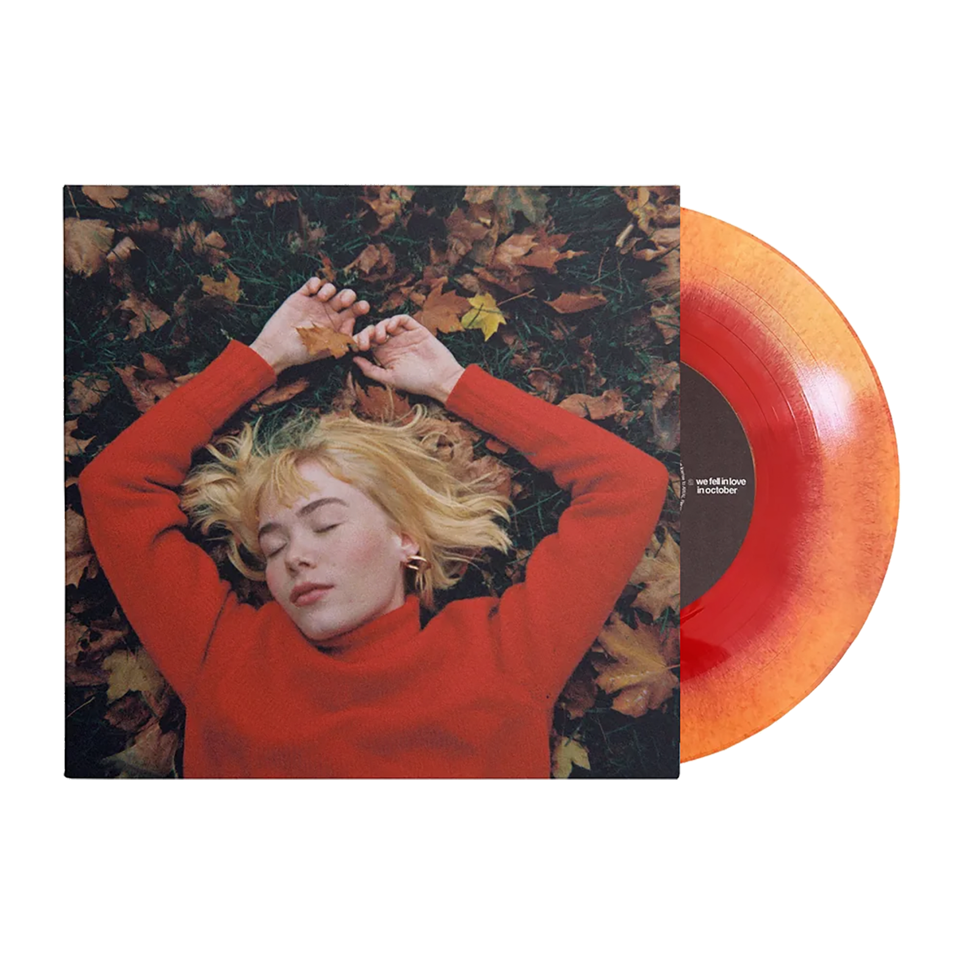 A person lying on leaves with their hands above their head, wearing a red sweater, with a orange and yellow vinyl record alongside.