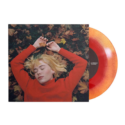 A person lying on leaves with their hands above their head, wearing a red sweater, with a orange and yellow vinyl record alongside.